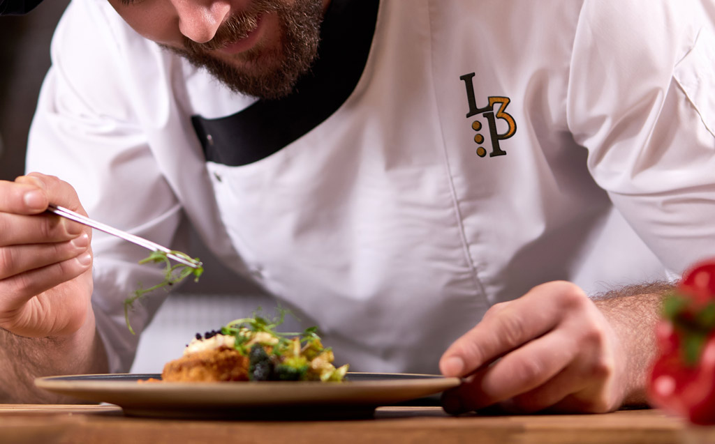 un cuisinier en plein dressage, le logo du restaurant semble brodé sur sa veste.